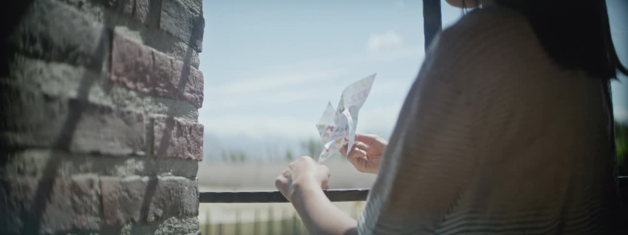 A young girl playing with a pin wheel standing in a window frame