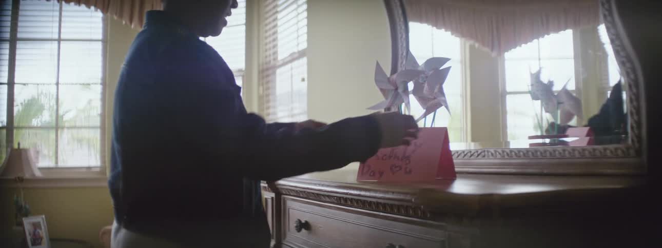A woman walks into her bedroom and reads a handwritten note on her dresser