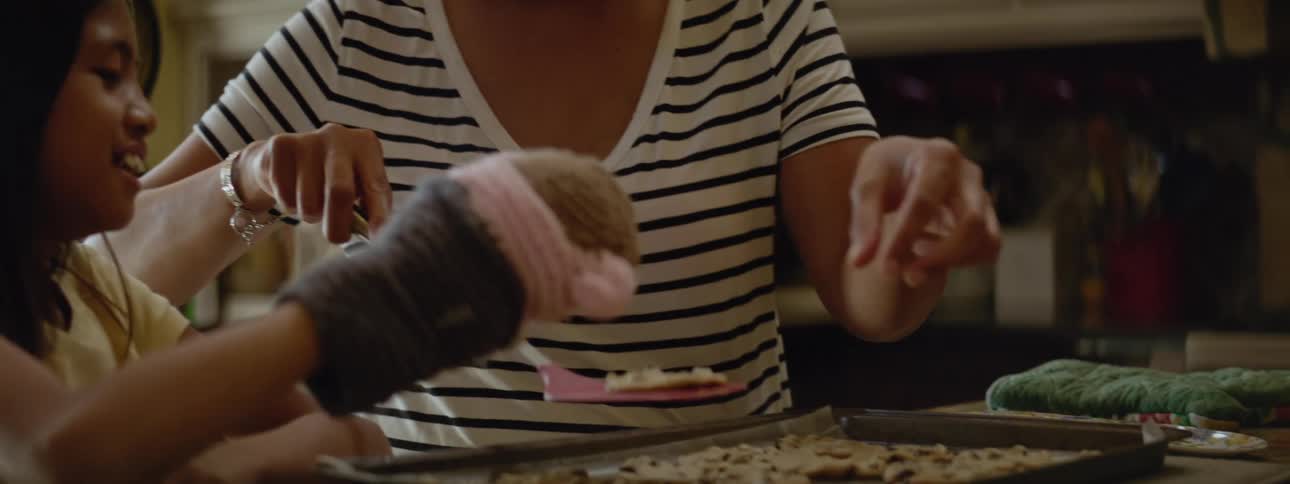 Young girl baking cookies in kitchen with grandma or mom laughing and smiling playing with puppet