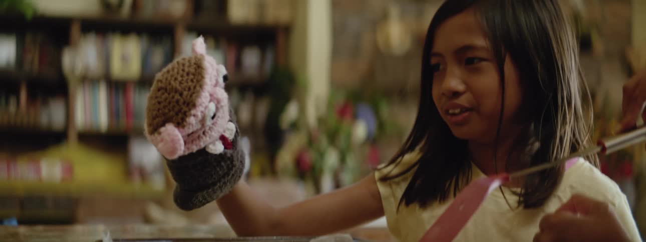 Girl plays with a puppet next to her mother baking cookies at home