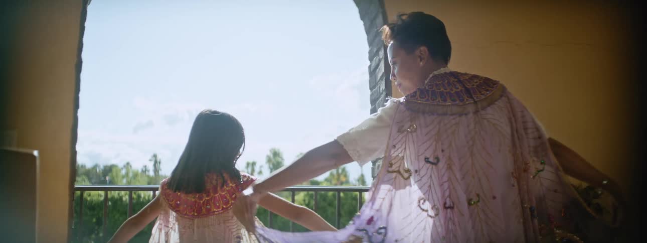 A grandmother and granddaughter play with dress capes at an open balcony in the day