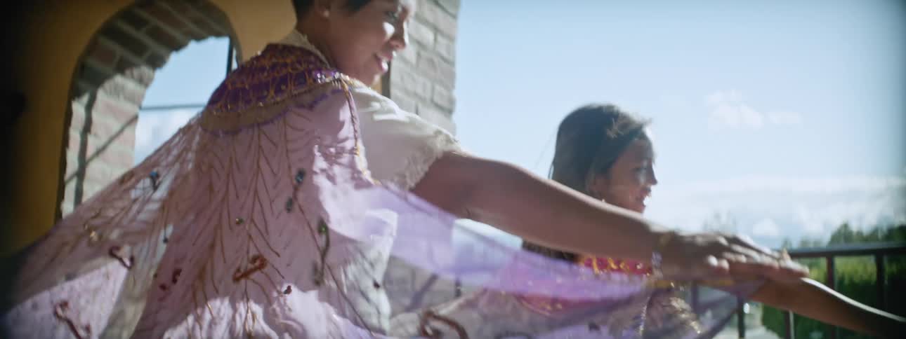 A mother and her daughter stand in front of a balcony railing letting the wind their dresses