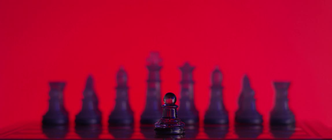 Close up of a pawn standing in front of the opposing pieces in front of a red background
