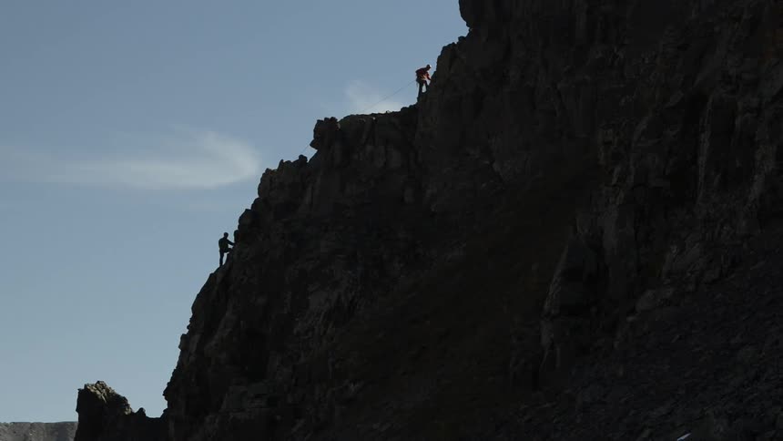 Silhouette of two mountaineers climbing the rocky slopes of a mountains under a blue sky