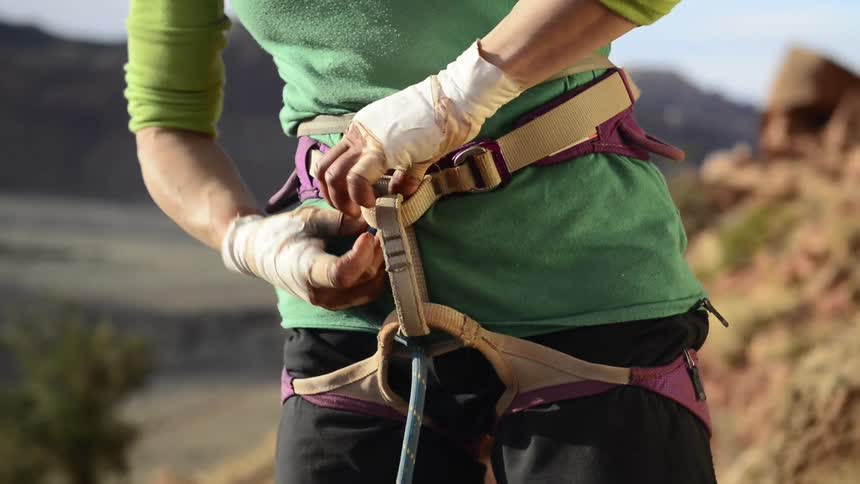 Female climber standing on mountain slope connects rope to her harness