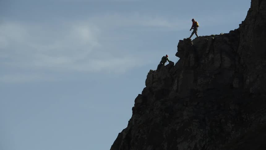 Silhouette of two mountaineers climbing the rocky slopes of a mountains under a blue sky