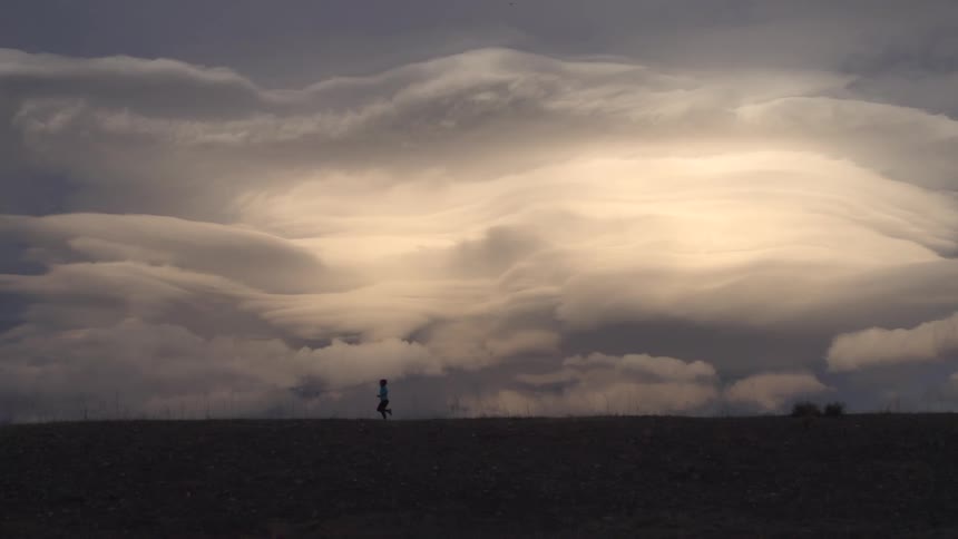 A silhouette of a person running on a glad land with a cloudy gray sky behind them