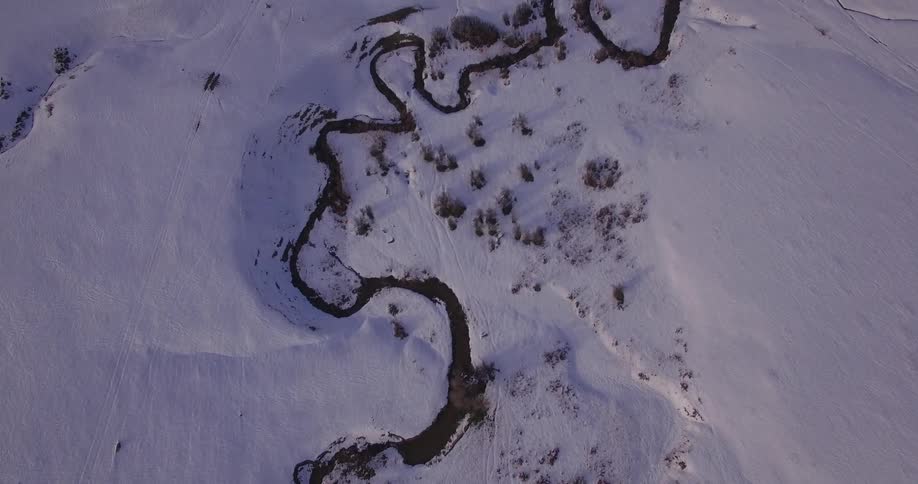 Top down aerial view of a winding river flowing through the plains covered in snow