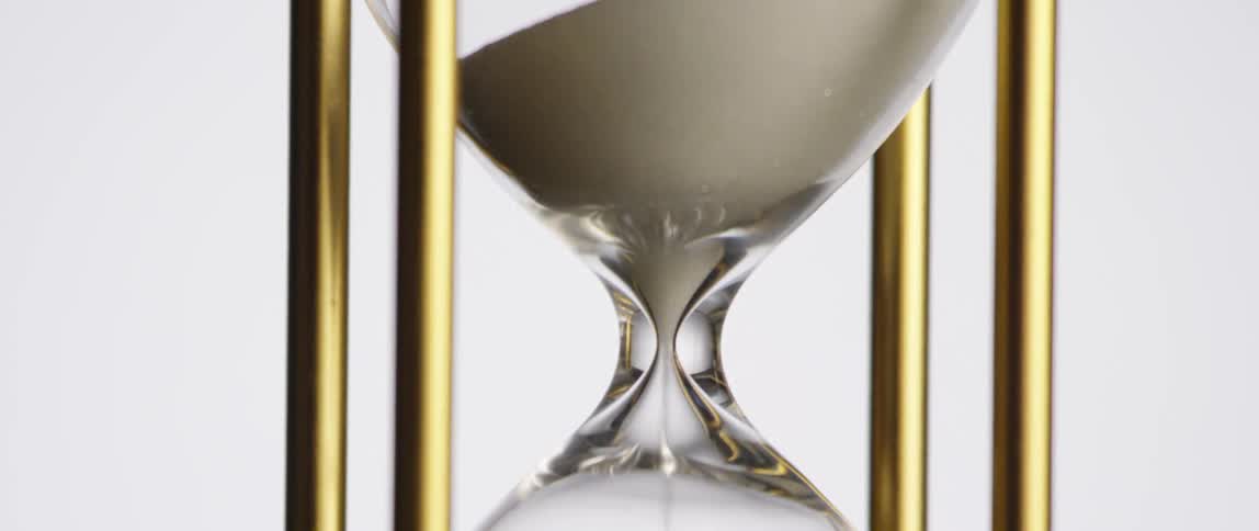 An hourglass gradually coming out of silhouette with sand trickling down about halfway through