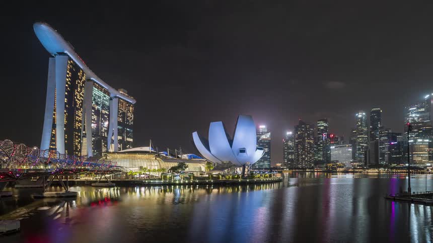 People move about on the waterfront near brightly lit modern architectural buildings in Singapore at night