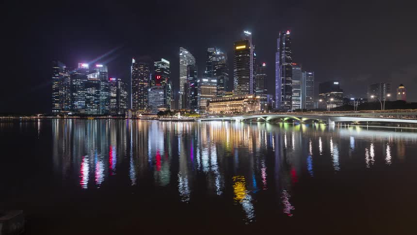 A time lapse of a city skyline at night with a water way reflecting the front of the tall buildings