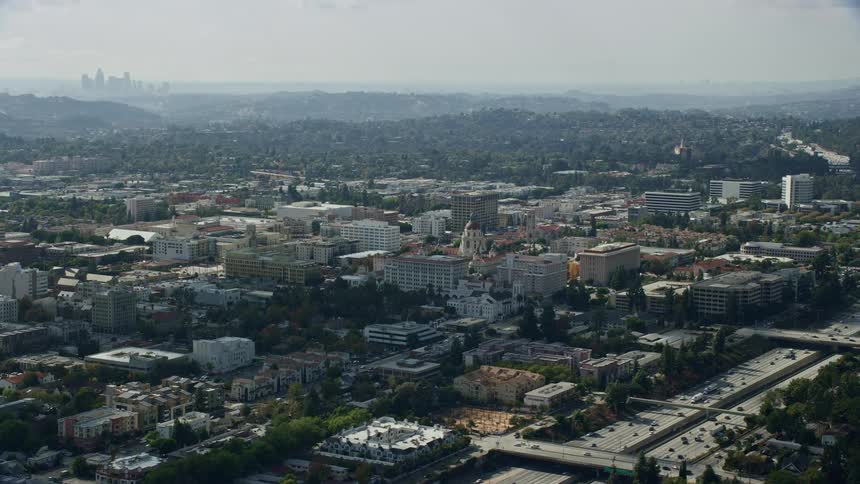 An orbiting aerial view of Pasadena City Hall and the Downtown Los Angeles skyline on a partly cloudy day in Southern California