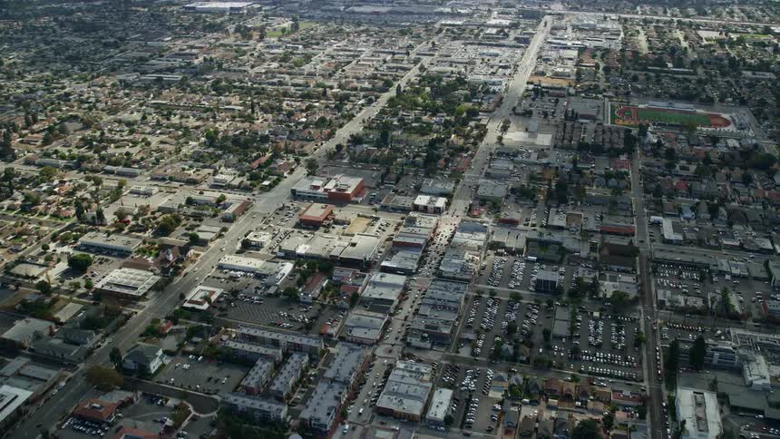 This is a aerial footage of Covina California showcasing city streets stores and residential neighborhoods on a partly cloudy day