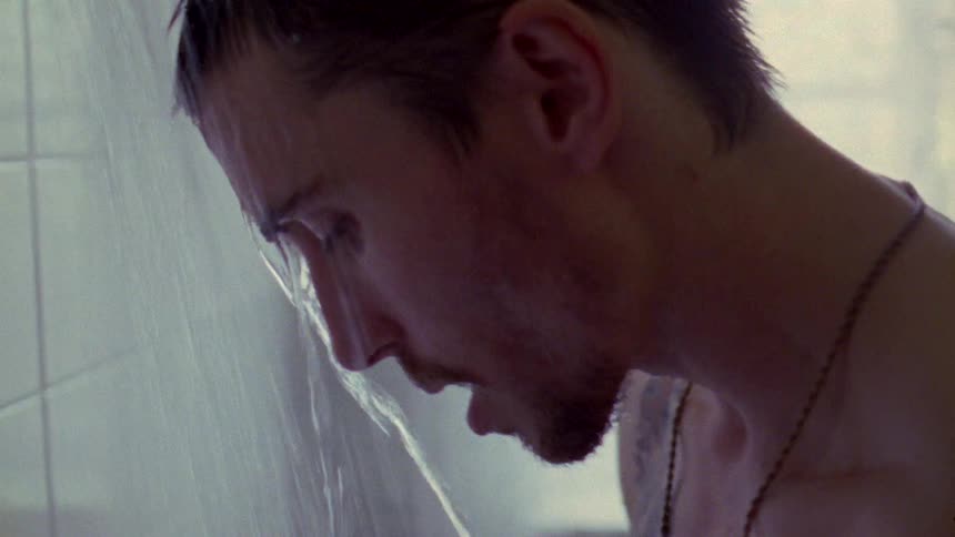 A side profile of a mans face while shower water runs down it and he looks at the floor