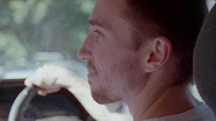 A close up of a side profile of a mans face as he looks to the left slightly smiling while driving a vehicle