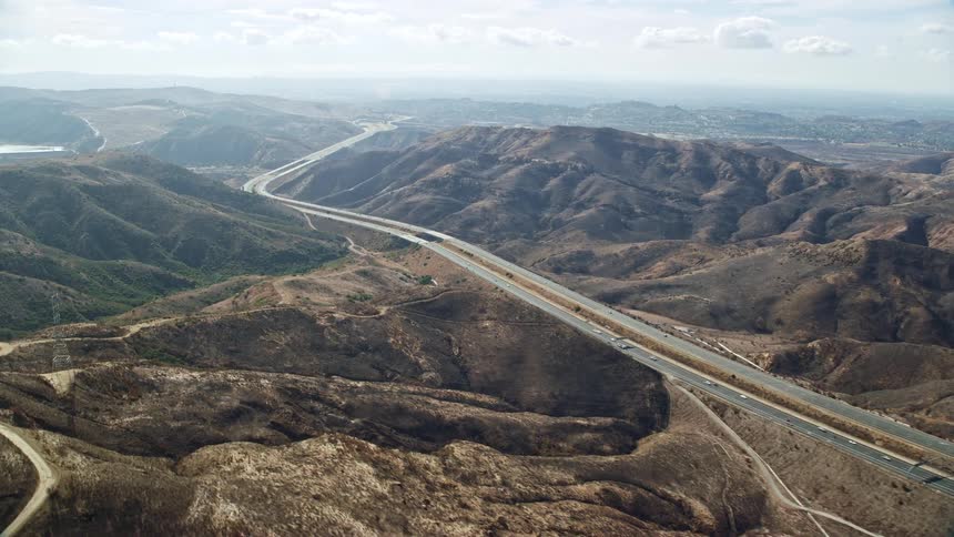 Aerial footage of several vehicles driving down a multi-lane freeway through hills in Anaheim California