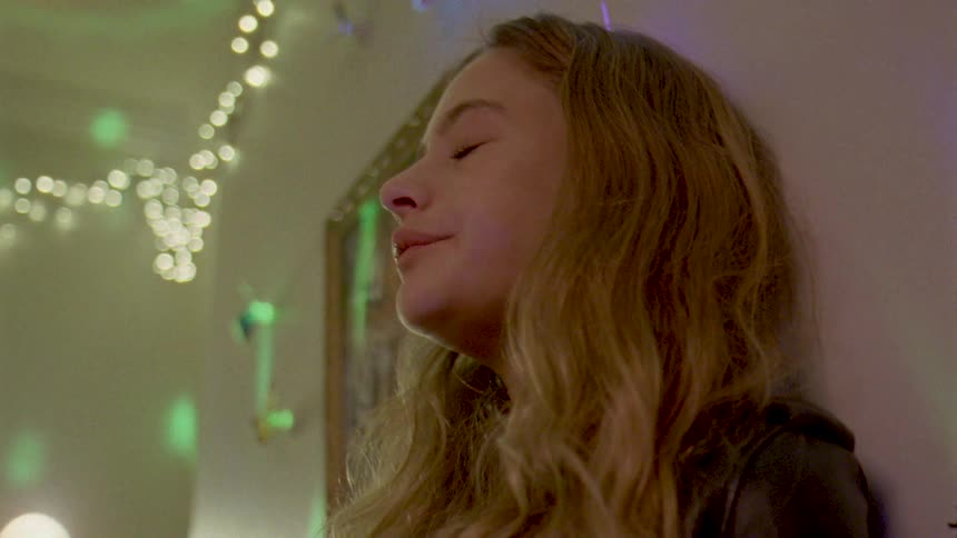 Young woman leaning against wall at party drinks then looks down sadly