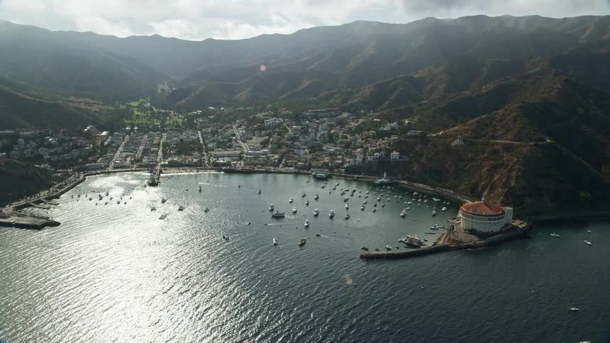 The clip features a breathtaking aerial view of the city of Avalon located on Santa Catalina Island with the harbor residences and industrial ports visible shot from a heightened altitude of during a partly cloudy day in California