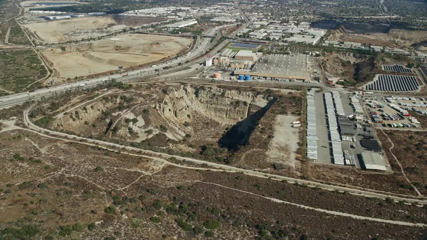 An epic aerial shot of an open pit next to a brewery in Irwindale California on a partly cloudy day during spring or summer
