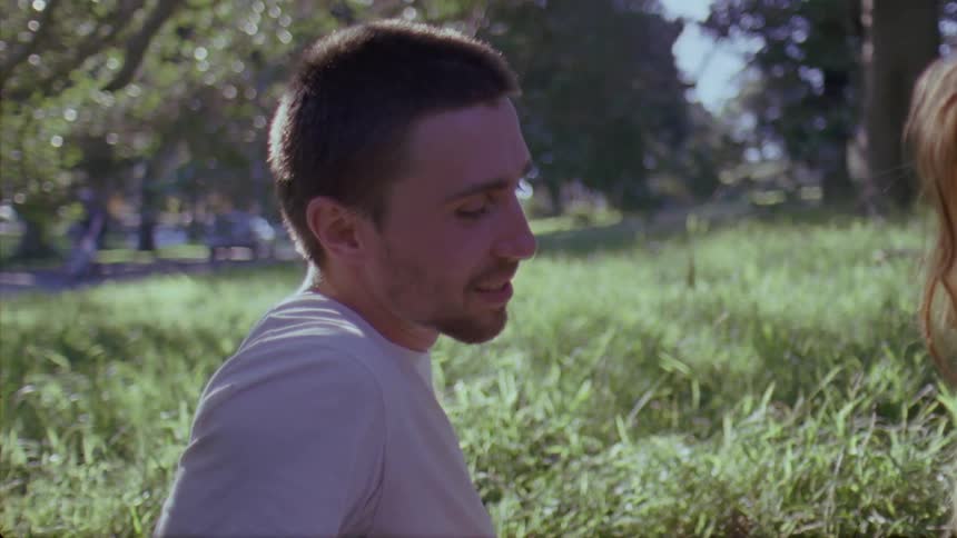 A man and woman sitting in grass looking at each other and smiling