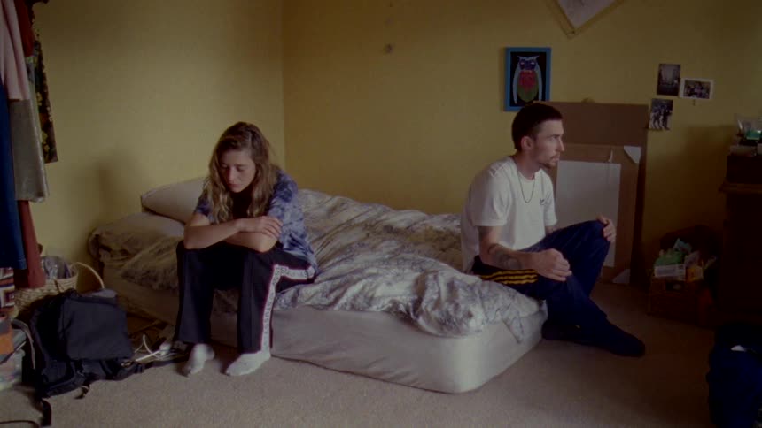 A couple sit on opposite sides of a mattress on the floor of their bedroom