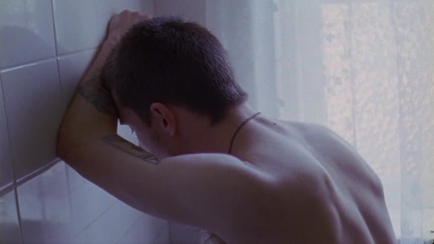 The backside of a man leaning up against a tile wall looking down at the floor