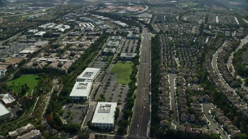 Aerial footage flying over Aliso Viejo Parkway in Southern California showing a highway running through the city during a partly cloudy summer day