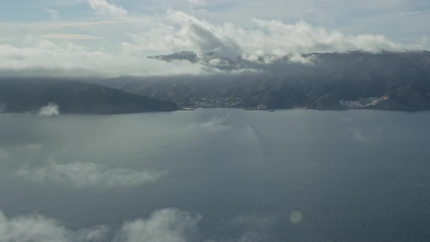 Aerial footage of Avalon on Catalina Island California showcasing the stunning shoreline and residential areas with partly cloudy skies and panoramic view of the West Coast