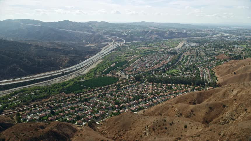 Flying over tract homes approaching the freeway in Yorba Linda California during the daytime with partly cloudy skies and a wide-angle shot