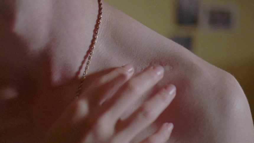 A close up of a womans body as she rubs her hand across a scar on her collarbone