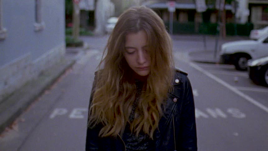 A teenage girl is sad as she walks on a neighborhood street passing parked cars