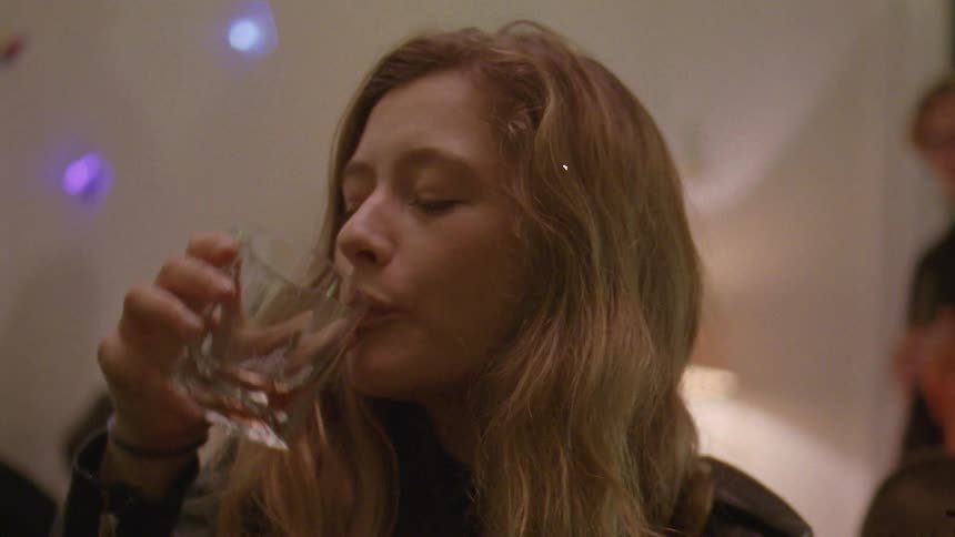 A close up of a young womans face with a sad expression as she drinks alcohol from a glass