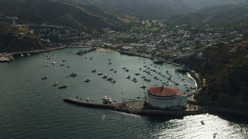 Aerial footage of boats anchored in Avalon Bay harbor next to the island town on Santa Catalina Island California on a partly cloudy day
