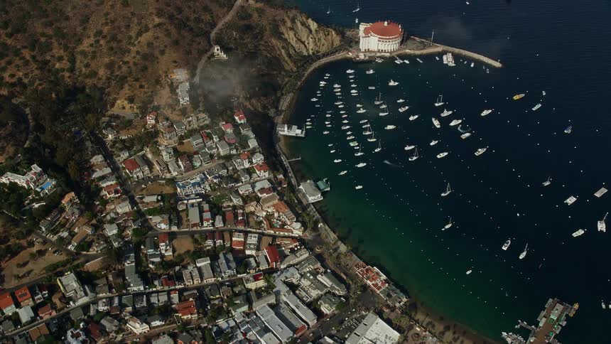  aerial footage captures stunning panoramic views of Catalina Island as the camera flies over clouds to reveal Avalon Harbor surrounded by epitomizing the quintessential seaside town