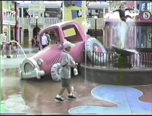 A boy with a hat and a spray bottle playing by a water fountain