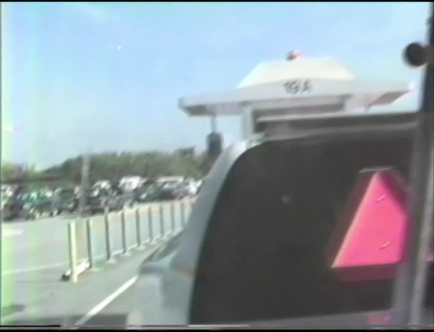 A young boy sits in the back of a boat being pulled a truck as it drives into a parking lot