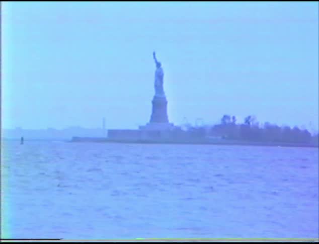 The statue of liberty on an island with the ocean in the foreground and the sky and clouds in the background
