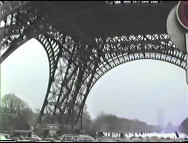 The eiffel tower with vehicles and people underneath with the sky and clouds in the background