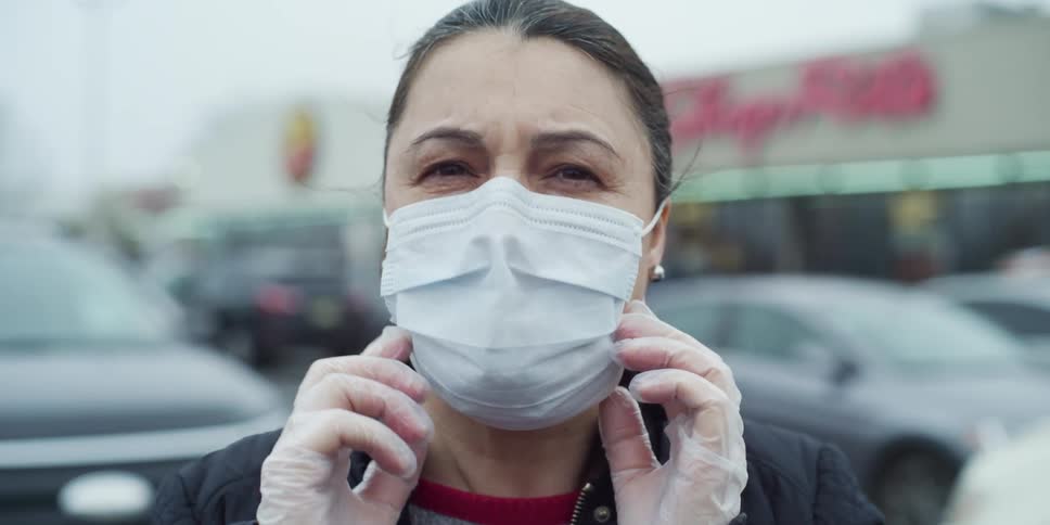 A woman with disposable gloves adjusting her mask in a parking lot