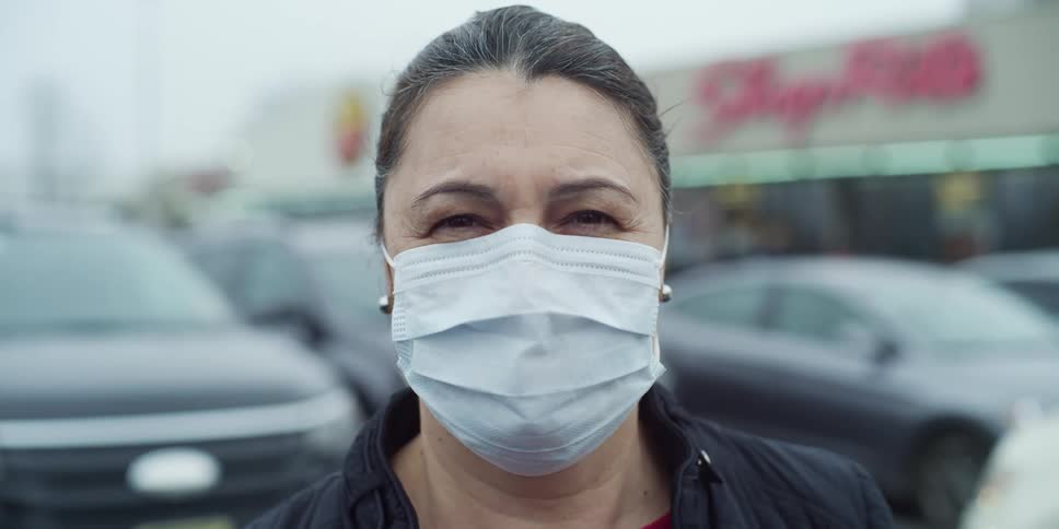 Woman wearing mask stands in parking lot outside a store