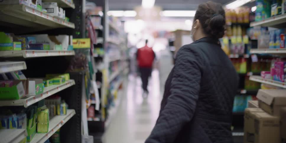 Woman wearing medical mask and gloves pulls cart through grocery aisle