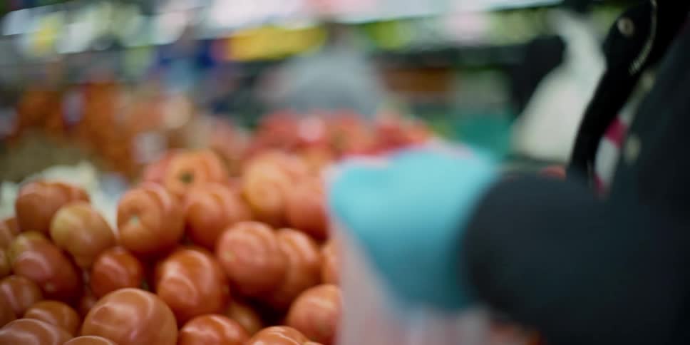 Woman wearing latex gloves buys tomatoes on supermarket