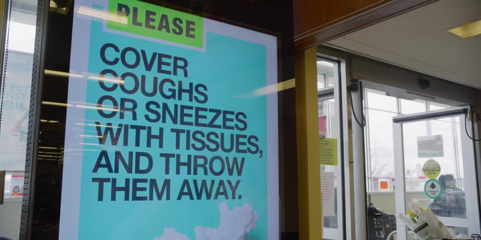 A large sign at a store asks people to cover their coughs and sneezes with tissue