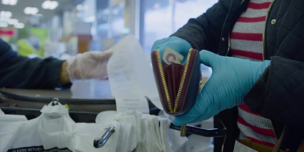 A woman with blue disposable gloves putting money into her purse