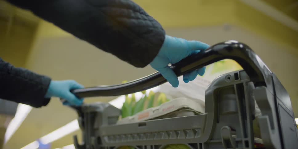 Person wearing latex gloves pushes shopping cart full of groceries on supermarket