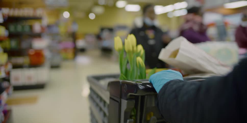 A person with disposable gloves pushing a shopping cart in a grocery store