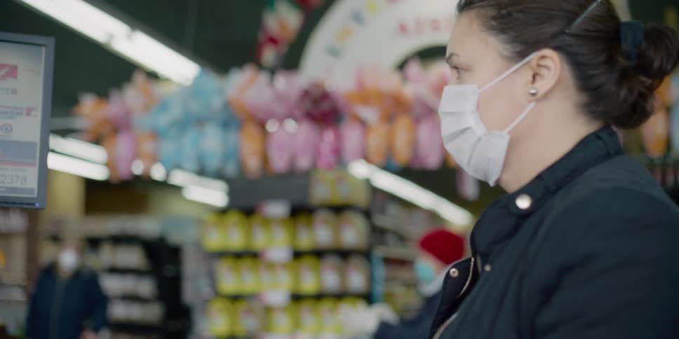 A woman wearing a mask walks up to the checkout counter at a grocery store