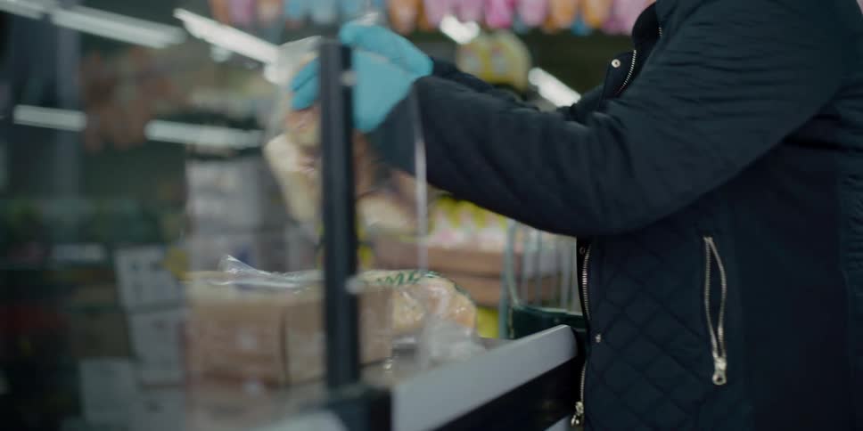 A woman wearing a mask and gloves places items from a shopping cart on the check out counter