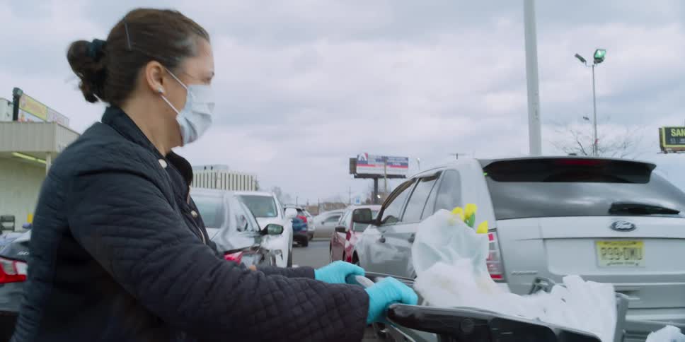 A woman with a mask pushing a shopping cart in a parking lot