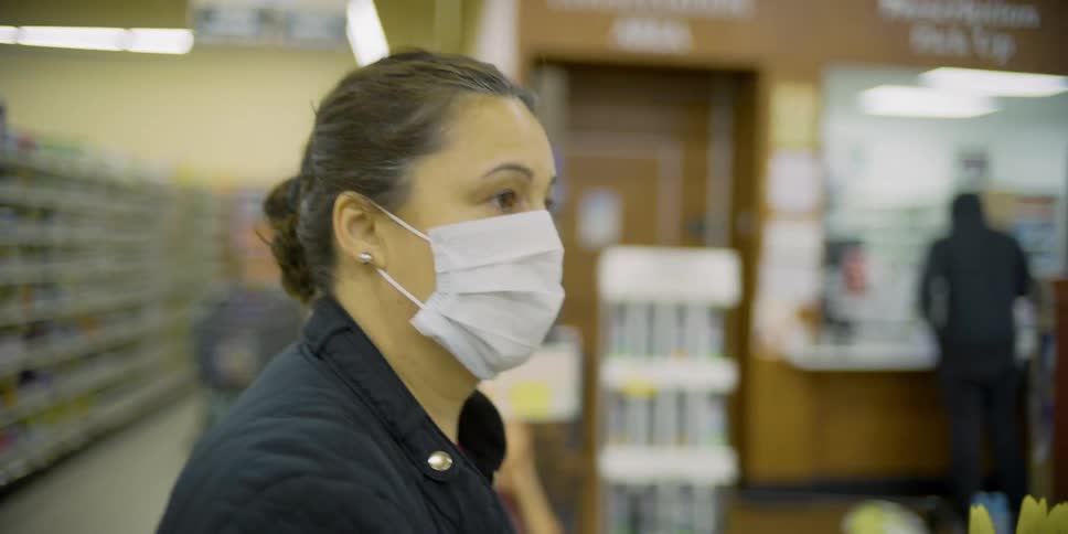 Woman wearing mask and jacket pushes cart through grocery store